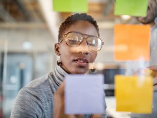 Black woman writing on sticky note on a transparent wall