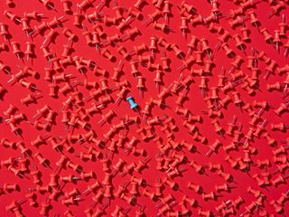 Blue thumbtack in a crowd of red thumbtacks