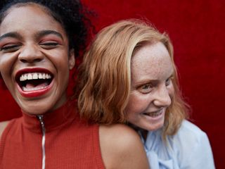 Close-up of two women laughing while standing against red wall