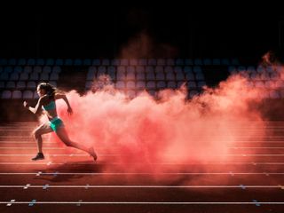 Female athlete unning on a race track and leaving behind a trail of red smoke