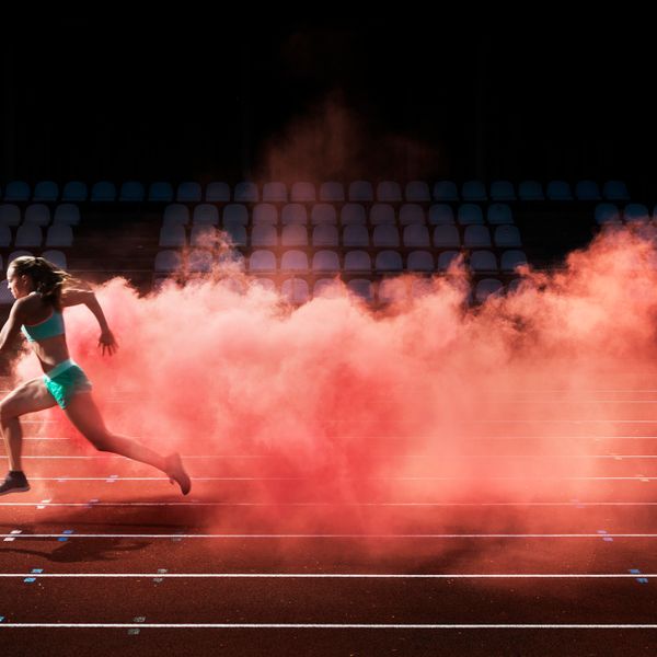 Female athlete unning on a race track and leaving behind a trail of red smoke