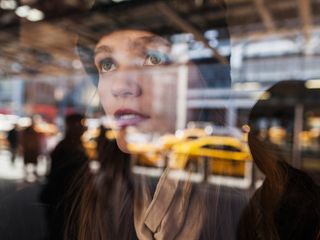 Girl looks through a glass window at taxis and people in New York City