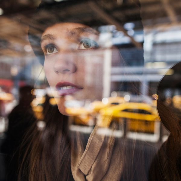 Girl looks through a glass window at taxis and people in New York City