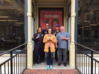Group of 4 people holding trophies and the word "Comrade" in the backgroud