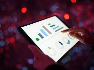 Hands holding a tablet displaying graphs