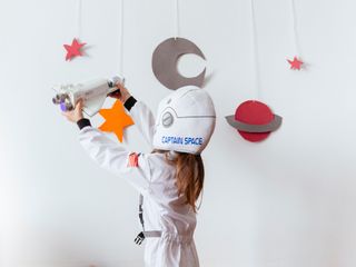 Kid wearing space suit playing with rocket against wall