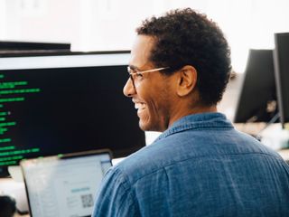 Male IT professional looking away while sitting in office in front of a computer