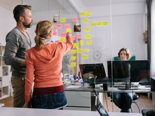 Man and woman looking at post-it notes on a glass wall