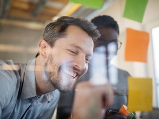 Man discussing with woman while writing on adhesive note