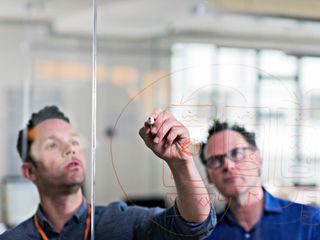 Man drawing diagram on glass wall in office
