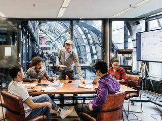 Man handing paper sheets out some to employees sat around a conference table