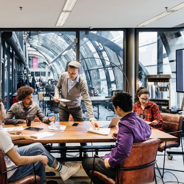 Man handing paper sheets out some to employees sat around a conference table