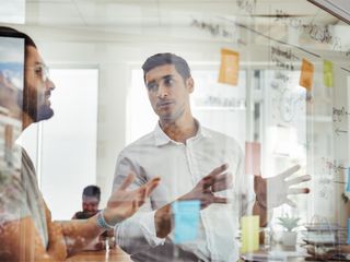Men brainstorming ideas and writing notes on a glass board