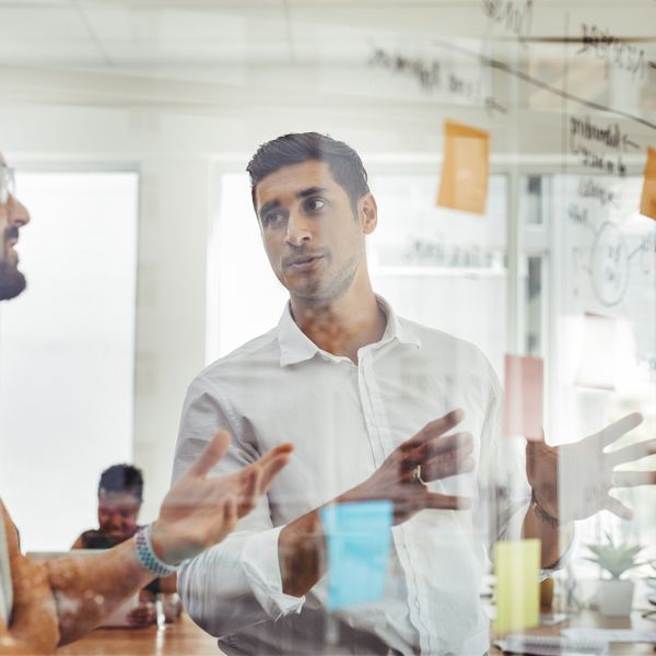 Men brainstorming ideas and writing notes on a glass board