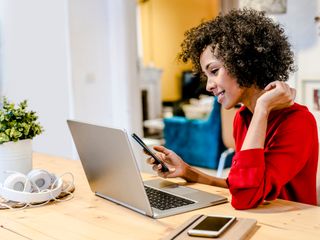 Smiling woman using laptop and cell phone at table
