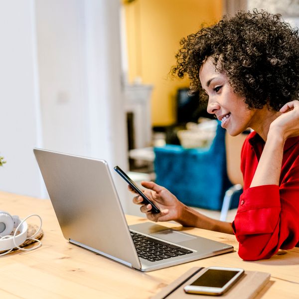 Smiling woman using laptop and cell phone at table