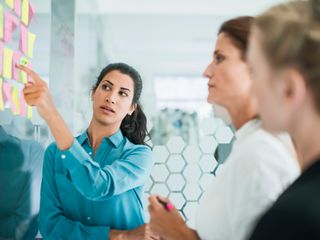 Three women in front of wall of stickers brainstorming