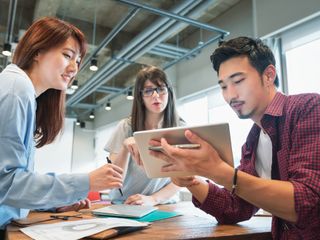 Two women and a man discussing over a tablet in modern office