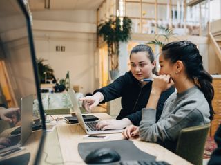Two women discussing on laptop while sitting in office