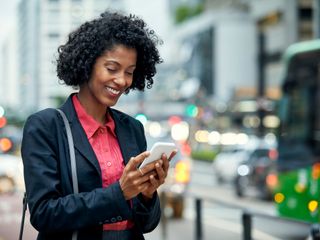 Woman smiling and holding a phone on a street