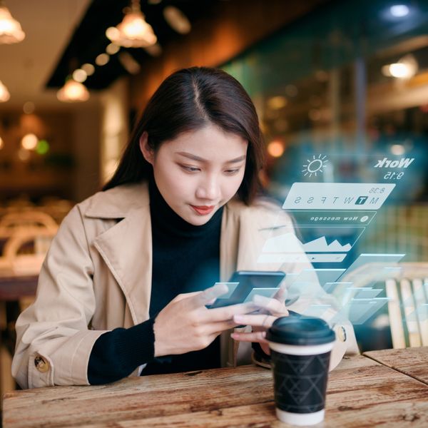 Woman uses mobile phone on virtual visual screen in cafe