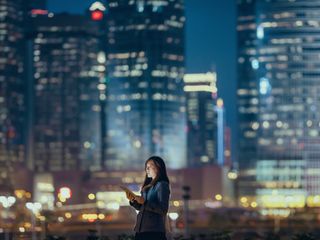 Woman using digital tablet against illuminated corporate skyscrapers at night