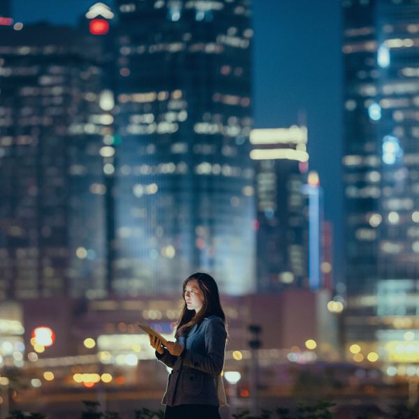 Woman using digital tablet against illuminated corporate skyscrapers at night