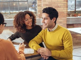 A couple smilling, meeting with a woman at a table reviewing some documents.