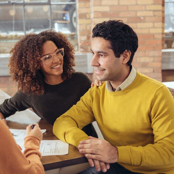 A couple smilling, meeting with a woman at a table reviewing some documents.