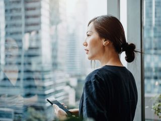 Businesswoman using smartphone in the office in front of a window overlooking the city