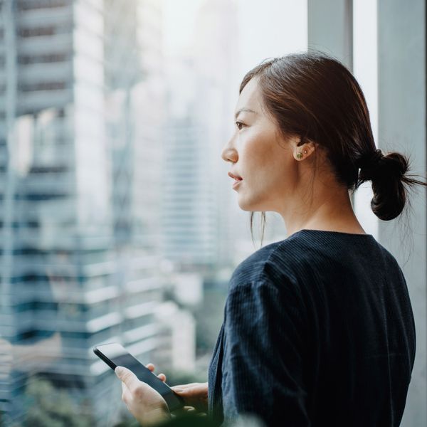 Businesswoman using smartphone in the office in front of a window overlooking the city