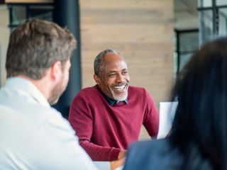 Homem sorrindo sentado com colegas em uma sala