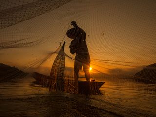 Silhouette of fishing boat and fisherman on sunset