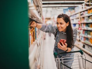 Woman in grocery story holding a phone and looking at products on a shelf