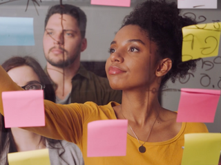 Woman writing on a glass board filled with sticky notes