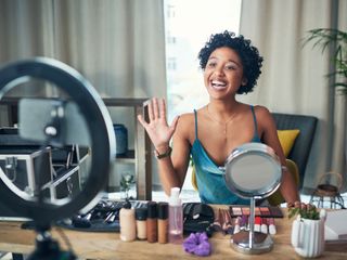A woman doing a makeup tutorial in front of a light ring and camera