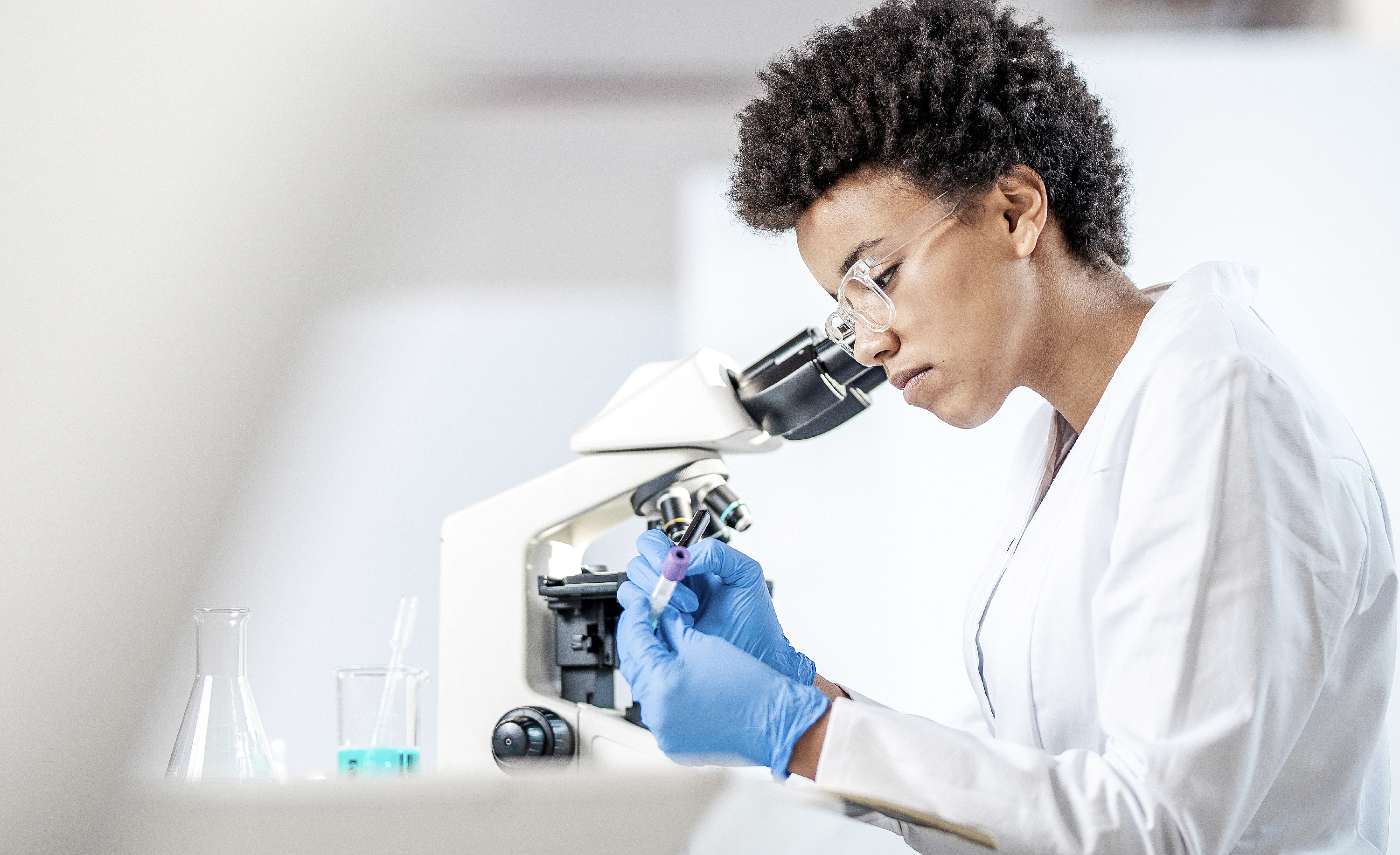 woman in a lab working on a microscope and marking a test tube