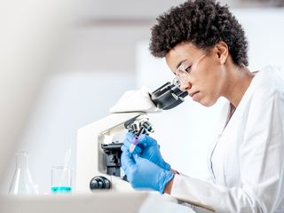 woman in a lab working on a microscope and marking a test tube