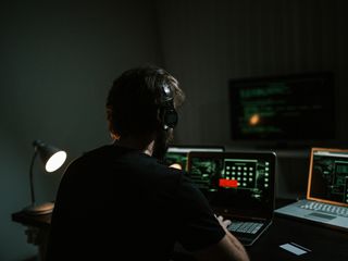Man working in a dark room using laptops and computers