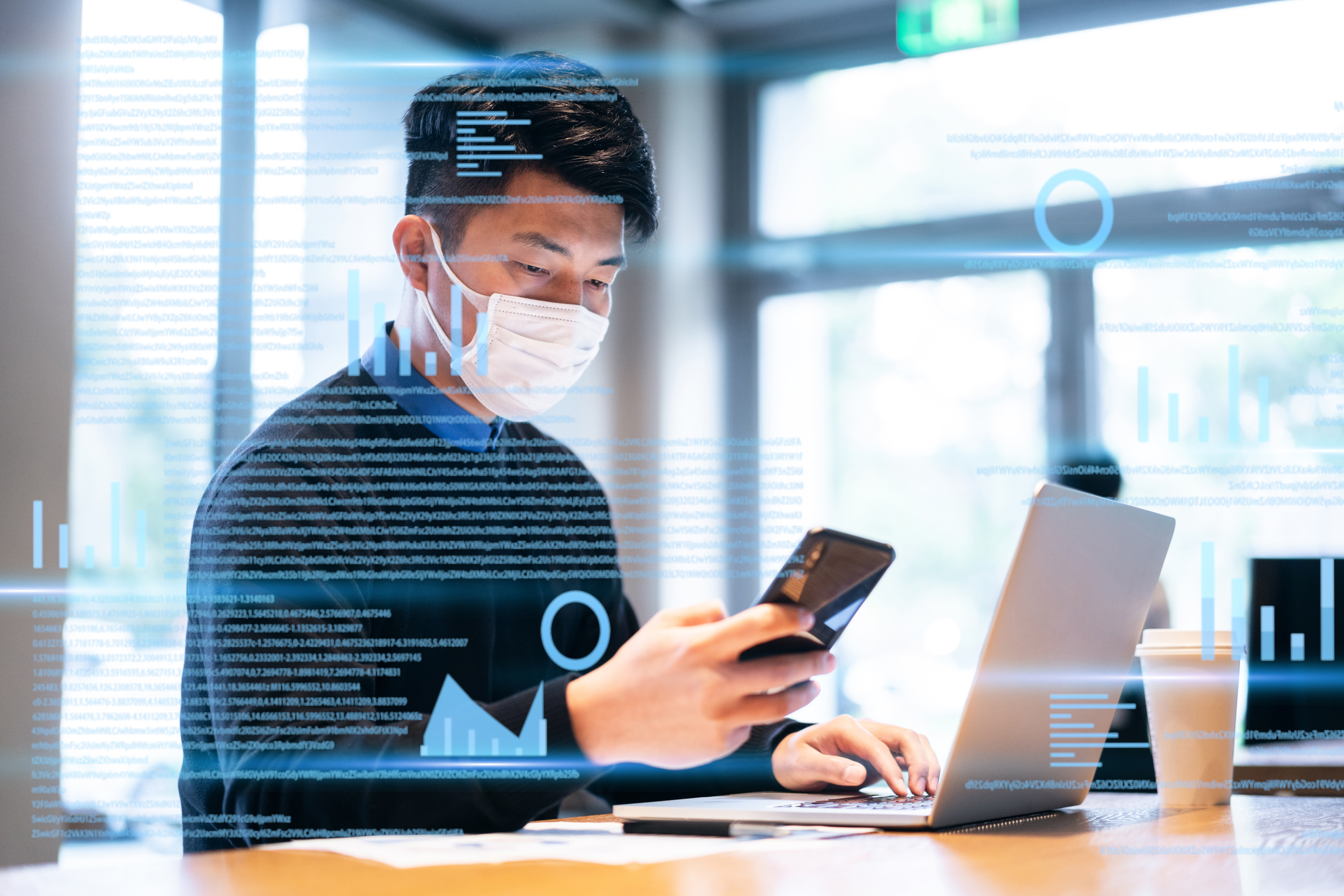 a man looking at a phone and working on data with laptop