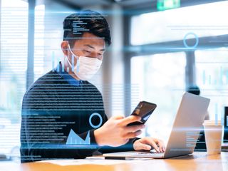  a man looking at a phone and working on data with laptop