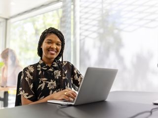 Mulher negra sorri sentada em frente ao computador