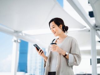 Woman looking to a phone and holding a cup of coffee