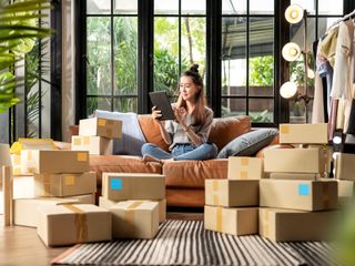 a woman sitting on her couch surrounded by boxes on her ipad