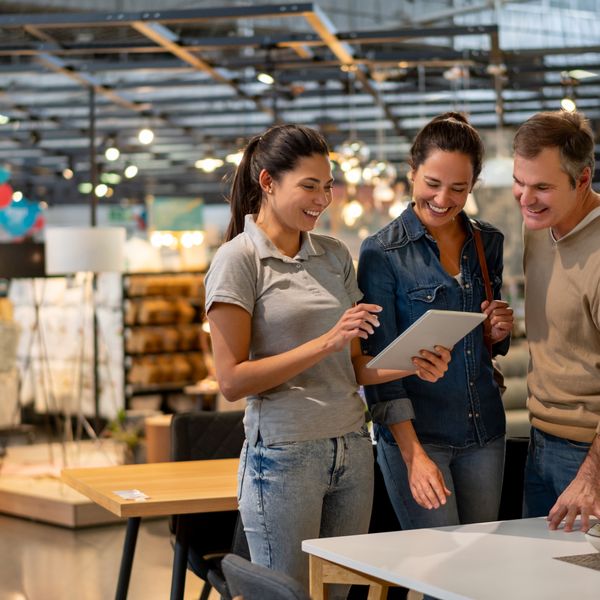 Cheerful sales woman showing a design on tablet to mid adult couple looking for furniture at a home store - Home renovation concepts