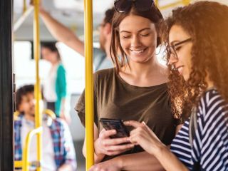 Two women standing on a bus holding their smartphones