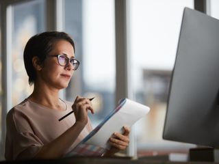 Woman holding a notebook while looking into a monitor