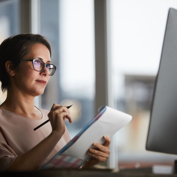 Woman holding a notebook while looking into a monitor