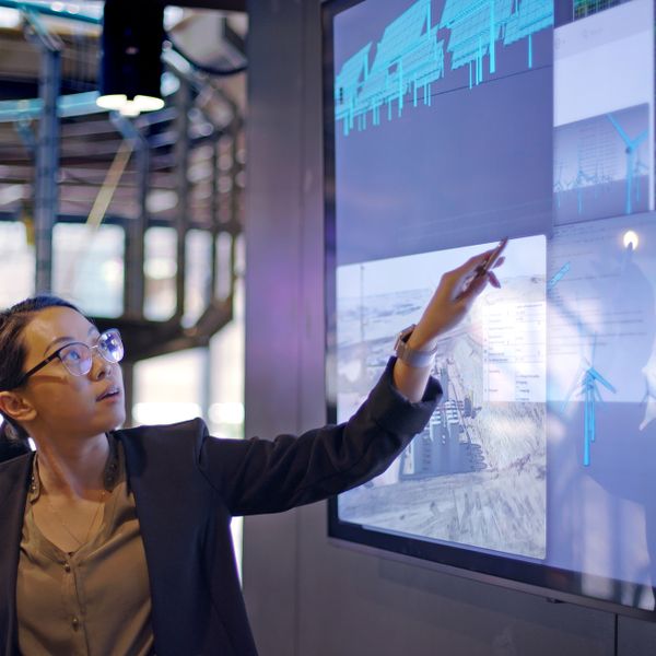 Woman lecturing in front of a big screen pointing to data charts