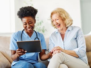 Nurse showing a tablet screen to senior woman and laughing at home